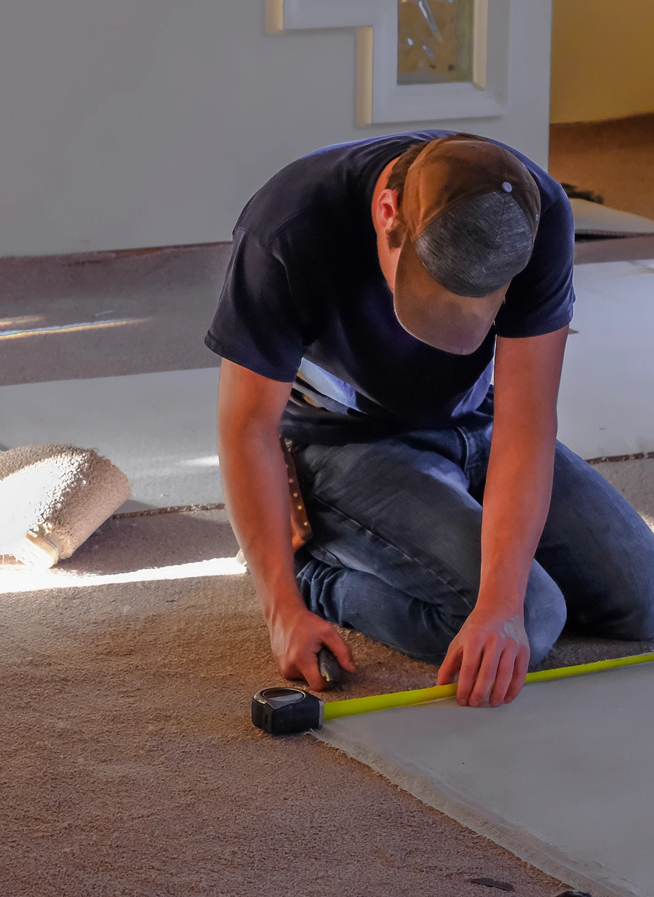 Person kneeling, preparing carpet for installation